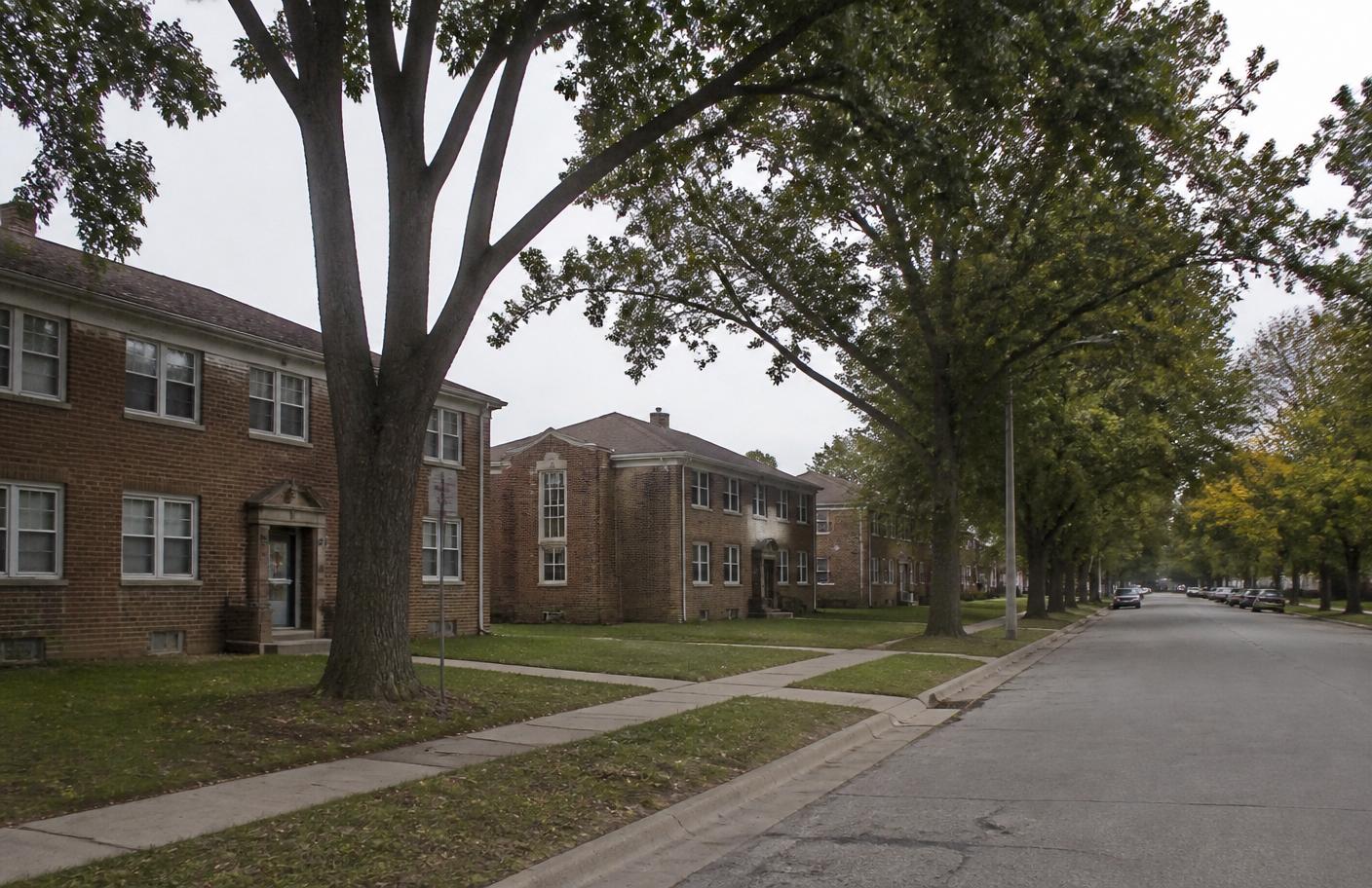 A quiet Michigan residential street with small brick apartment buildings and mature trees
